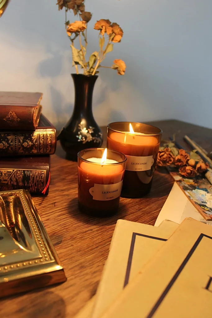 Photo de plusieurs bougies parfumées de la marque Klervi Paris, posées sur une élégant bureau en bois accompagnées de livres et de roses séchées